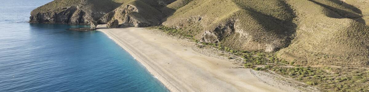 A coastal landscape with a sandy beach, clear blue waters, and green hills.