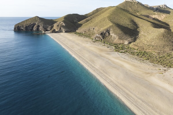 Un paisaje costero con una playa arenosa, aguas azules cristalinas y colinas verdes.