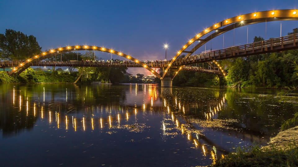 A bridge with lights reflecting on the water at dusk.