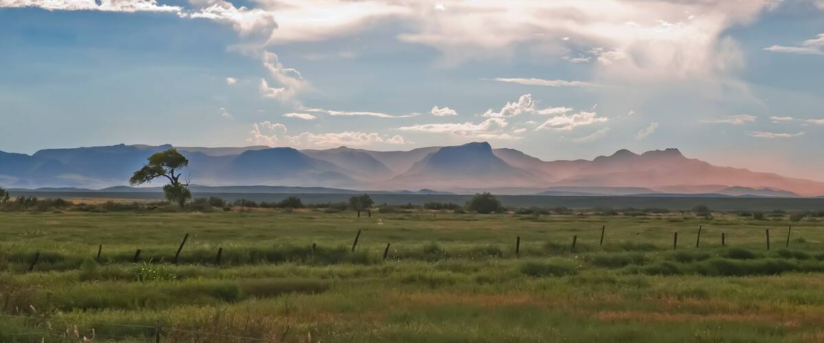 A grassy field with distant mountains under a partly cloudy sky.