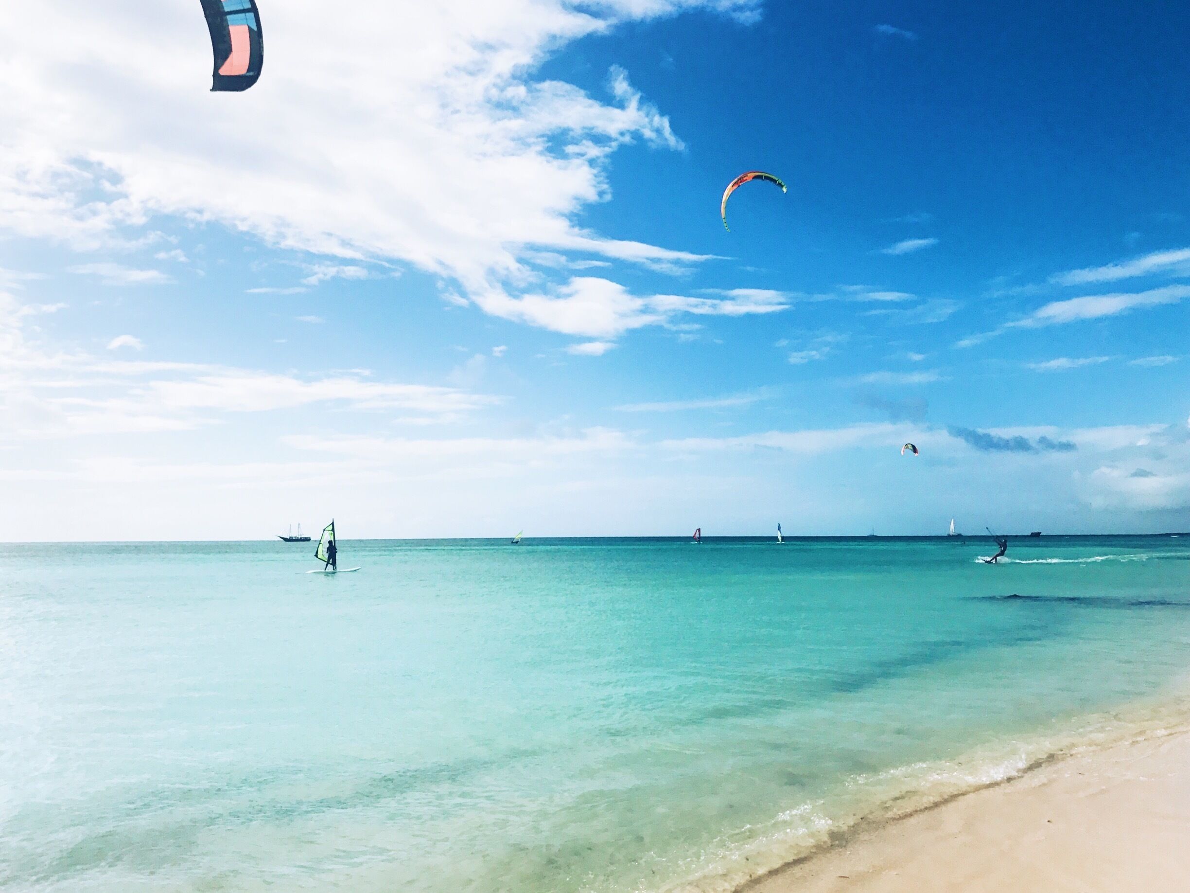A beach with clear turquoise water, a sandy shore, and several people windsurfing.