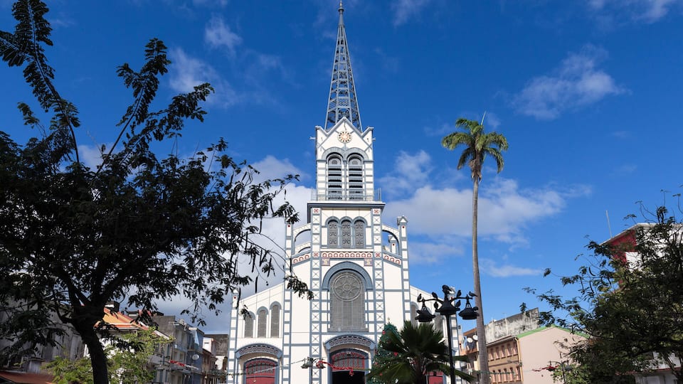 A church with a tall spire and a clock, surrounded by trees and buildings.