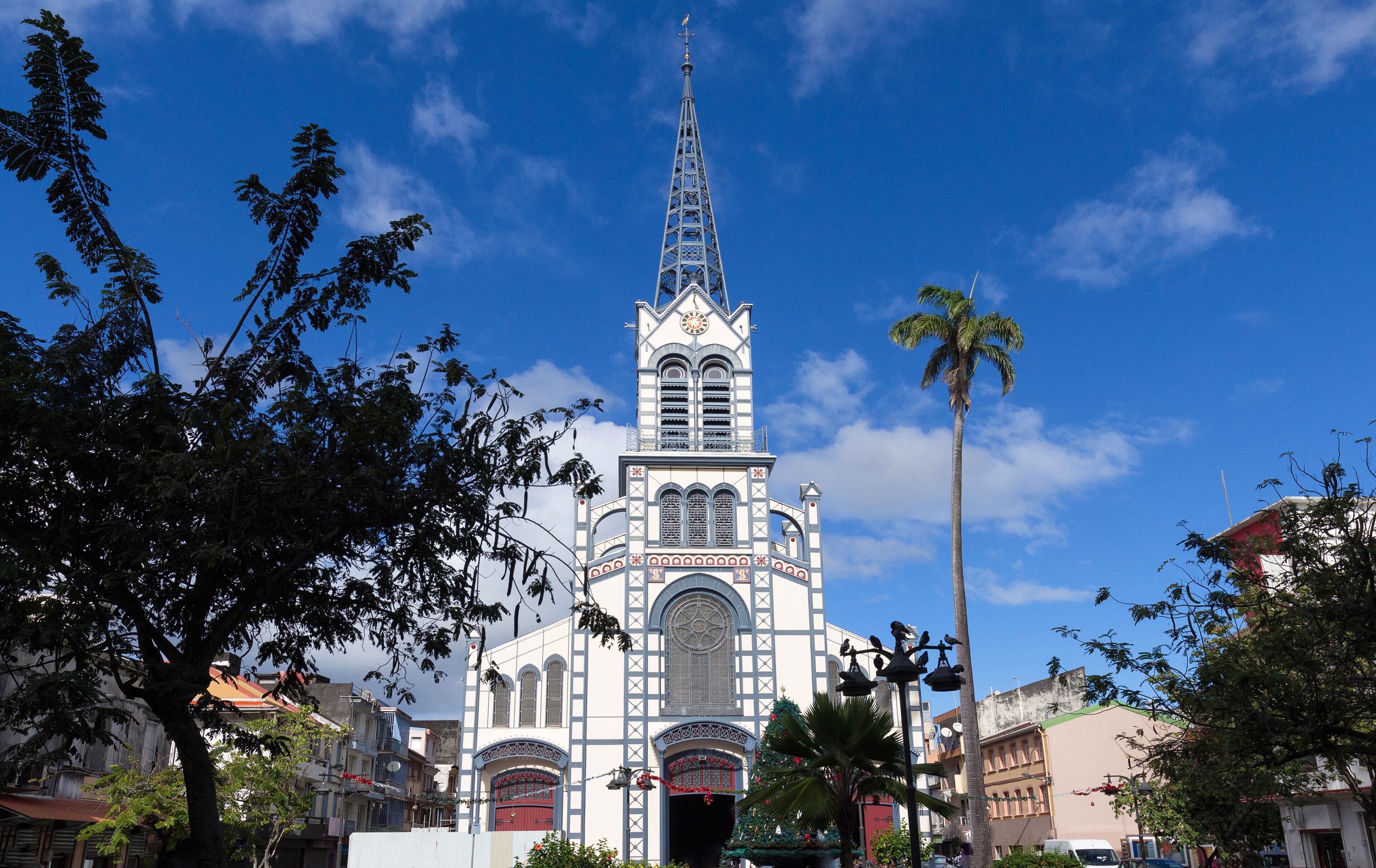 A church with a tall spire and a clock, surrounded by trees and buildings.