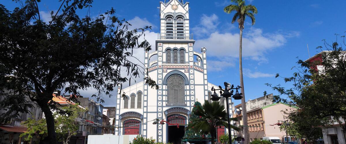 A church with a tall spire and a clock, surrounded by trees and buildings.