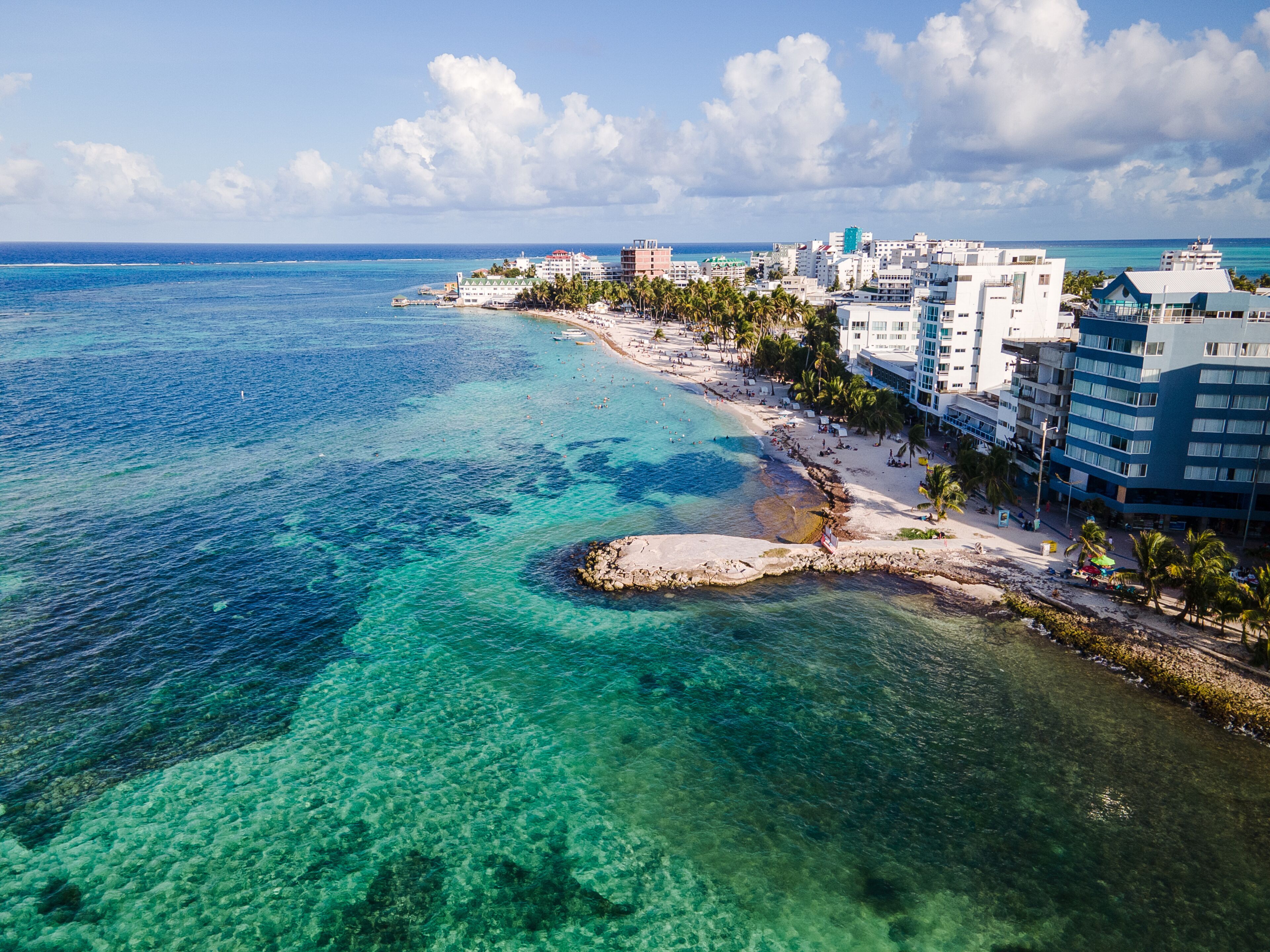 Una ciudad costera con mar azul cristalino, una playa arenosa y una hilera de edificios a lo largo de la costa.