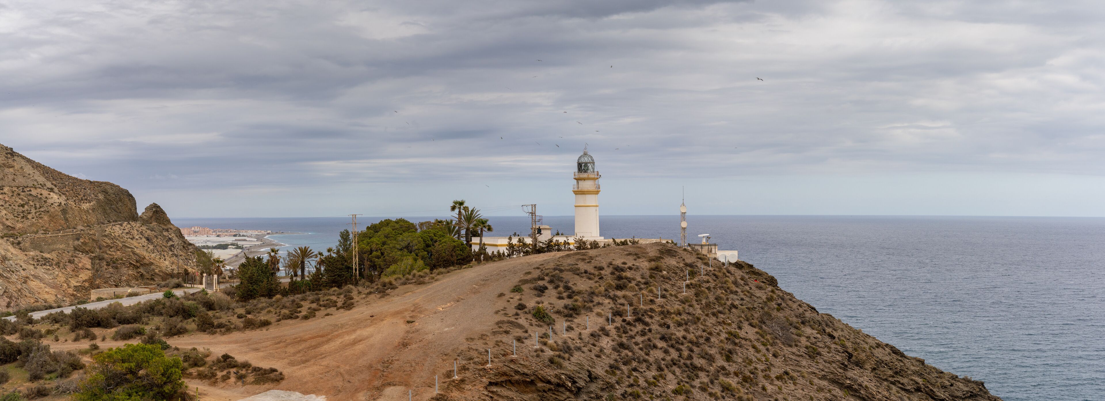 A coastal landscape with a lighthouse, rocky terrain, and a road leading to a beach.