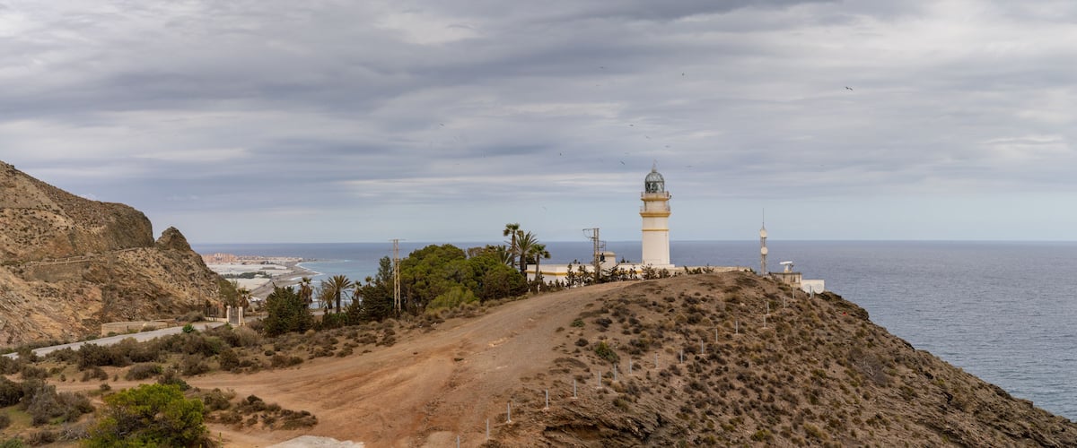 A coastal landscape with a lighthouse, rocky terrain, and a road leading to a beach.