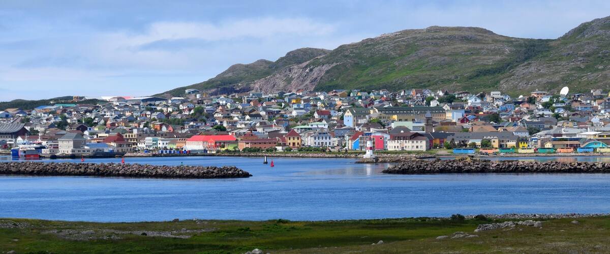 A coastal town with colorful houses, a rocky shoreline, and a hill in the background.