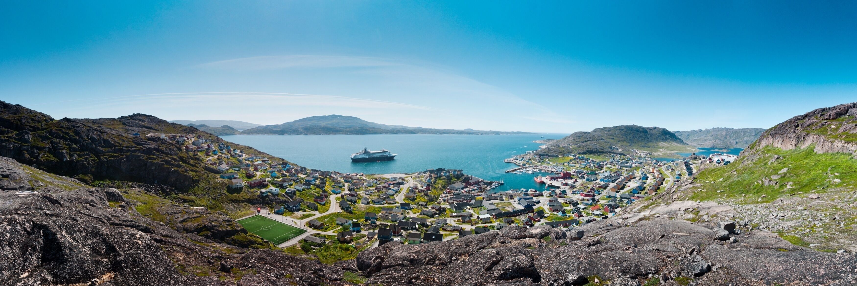 Panoramic shot of the coast at Greenland, Qaqortoq with a boat sailing in the sea