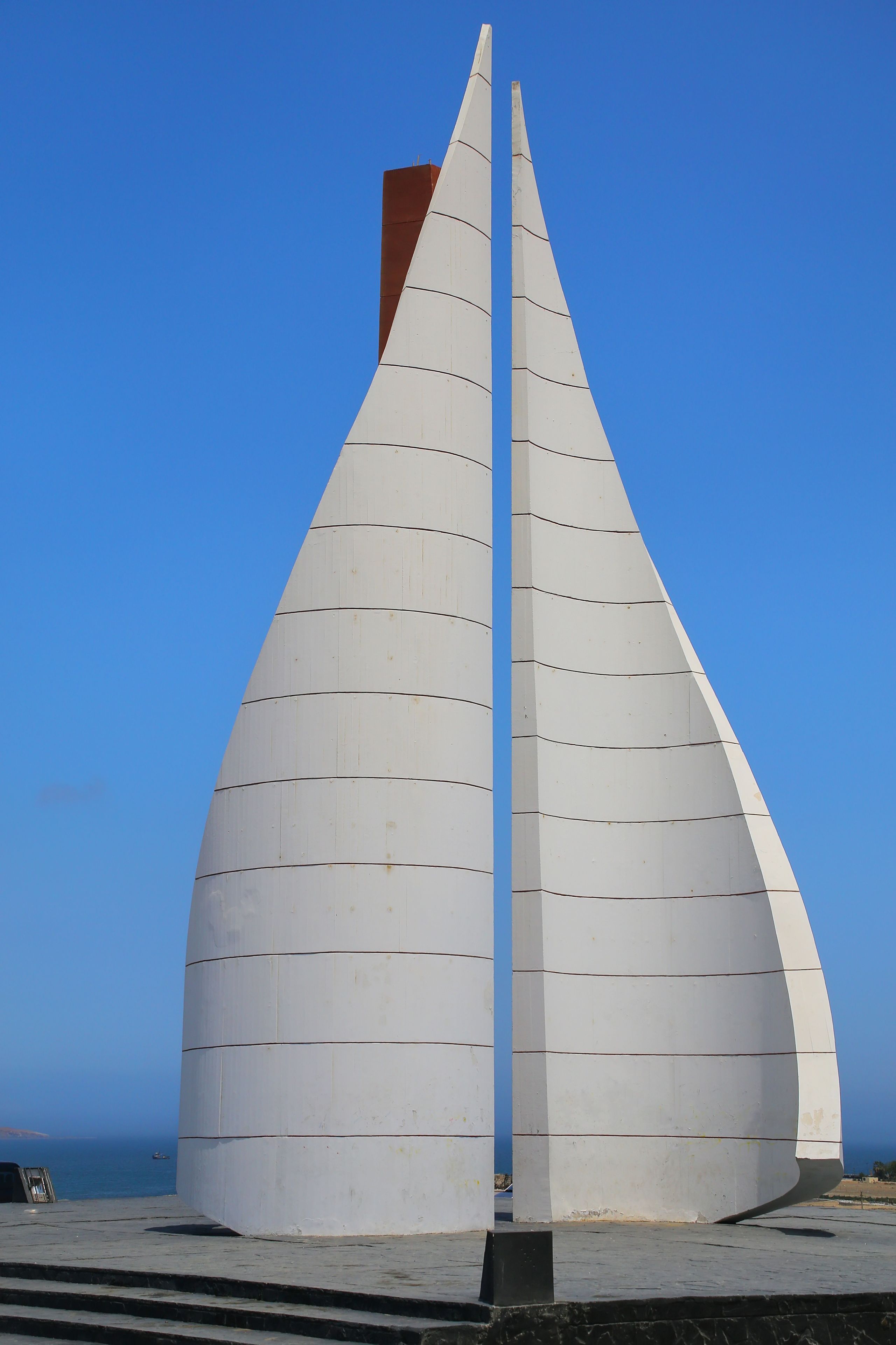 Una estructura blanca en forma de vela, con un mástil central, sobre un cielo azul despejado.
