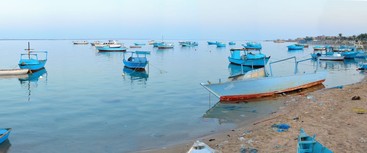 A beach with numerous small boats anchored in calm waters.