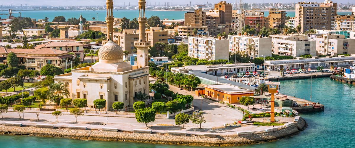 A coastal cityscape with a prominent mosque, a marina, and surrounding urban buildings.