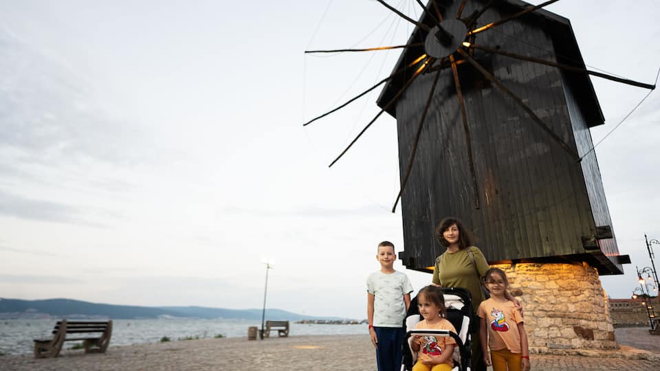 A windmill, a stone wall, a wooden bench, and a body of water.