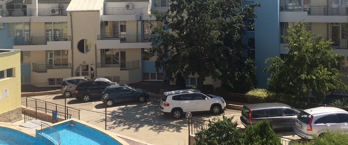 A residential area with a swimming pool, parked cars, and apartment buildings.