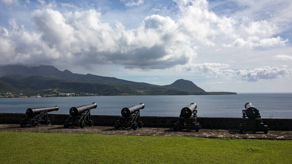 A coastal artillery battery overlooking a calm sea with mountains in the background.