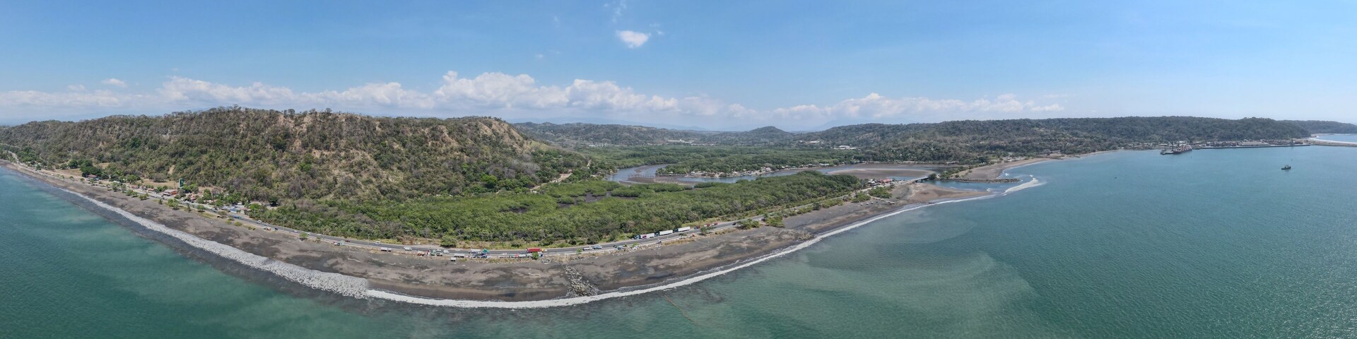 Vista aérea de una zona costera con una pequeña isla, una playa y un cielo azul despejado.