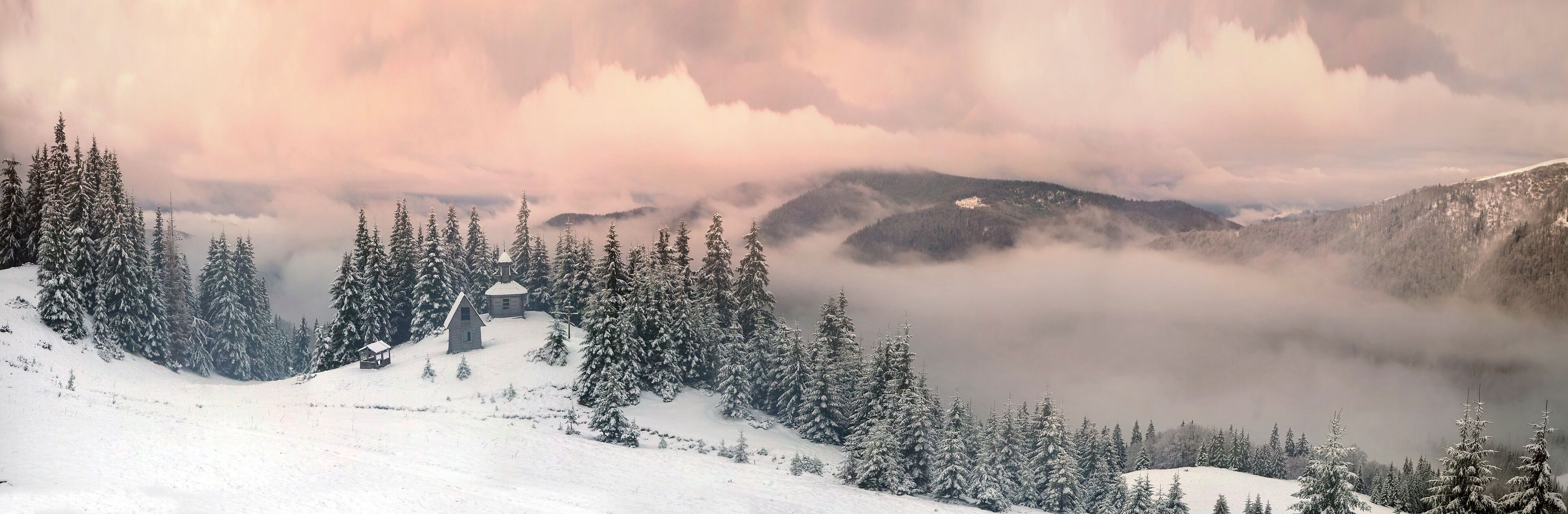 A snow-covered mountain landscape with a small cabin and dense evergreen trees.