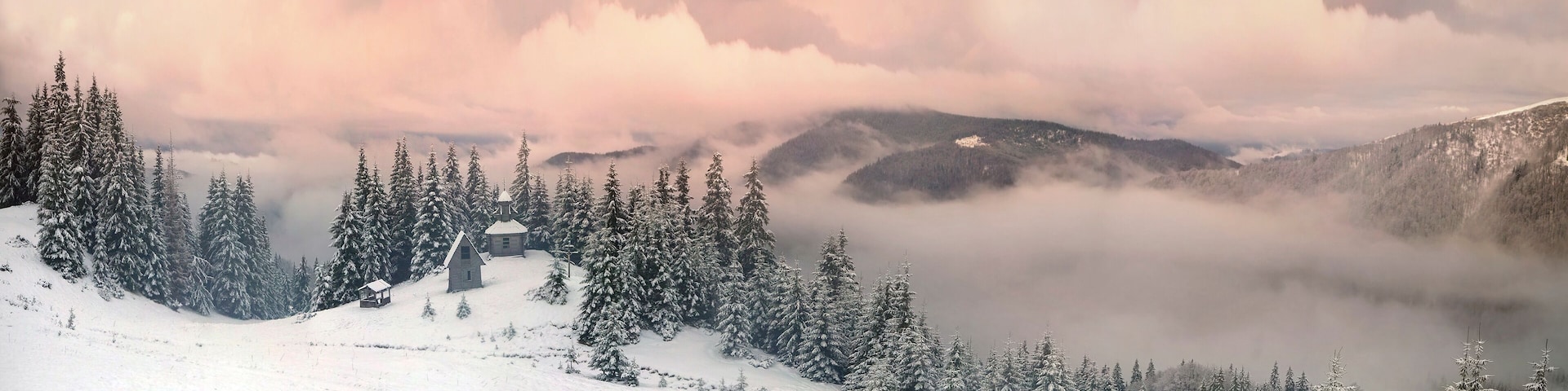 A snow-covered mountain landscape with a small cabin and dense evergreen trees.