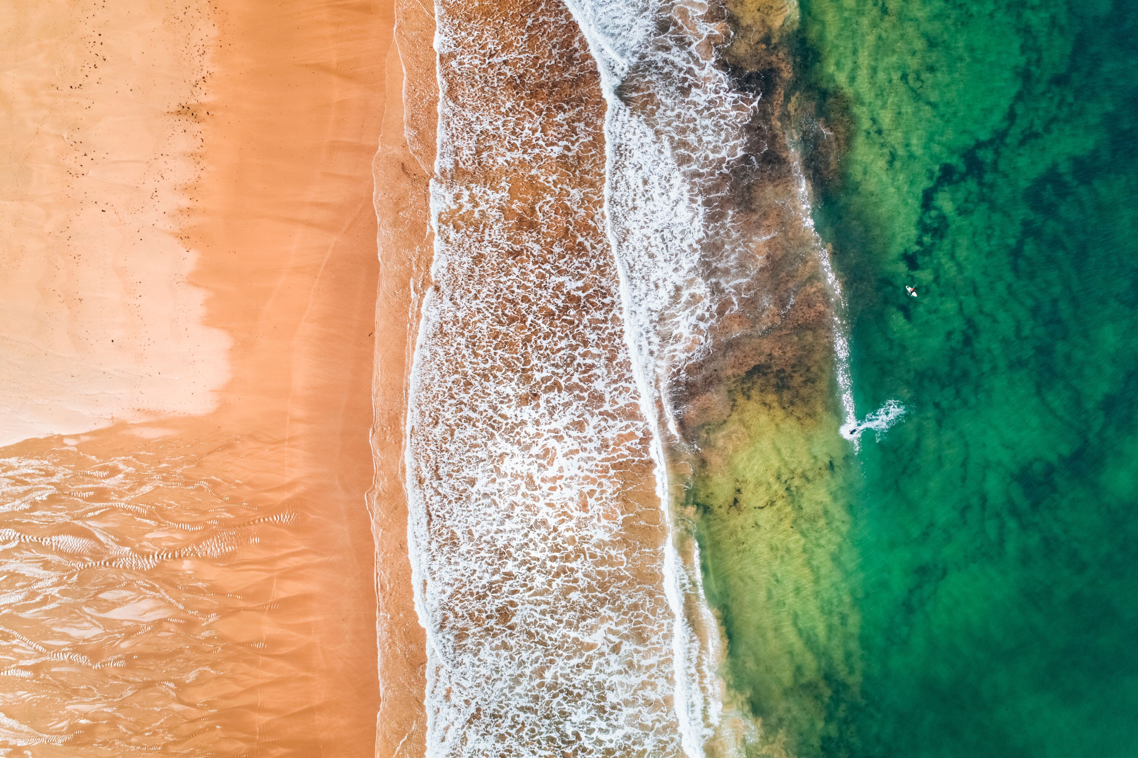 Vista aérea de una playa con agua turquesa cristalina, una orilla arenosa y un pequeño bote cerca de la orilla.