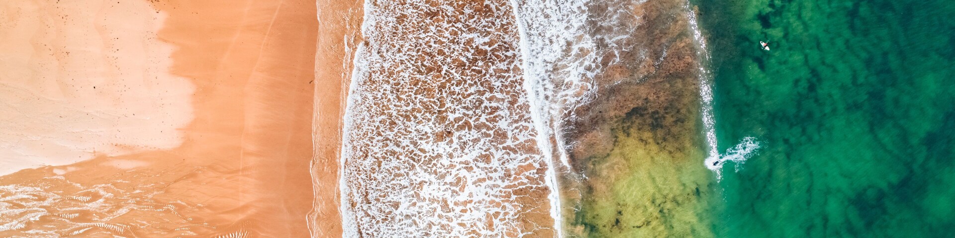 Vista aérea de una playa con agua turquesa cristalina, una orilla arenosa y un pequeño bote cerca de la orilla.