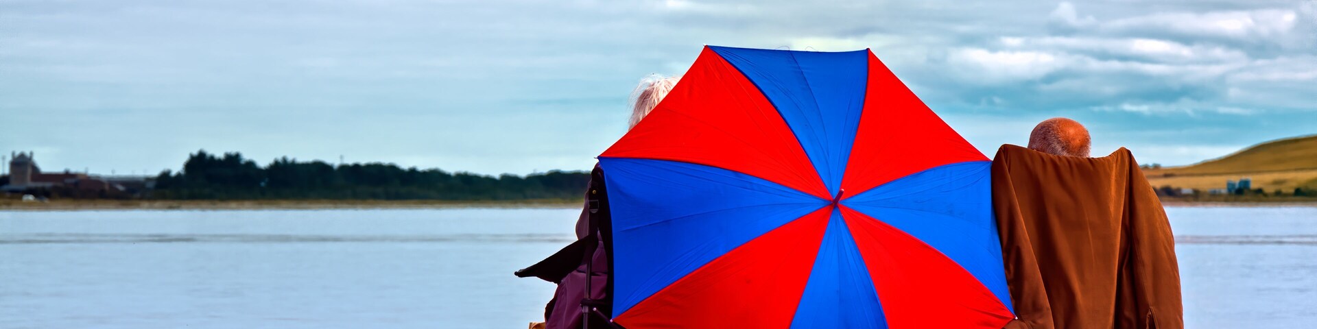 Una playa de guijarros con un paraguas grande y una persona con una chaqueta marrón.