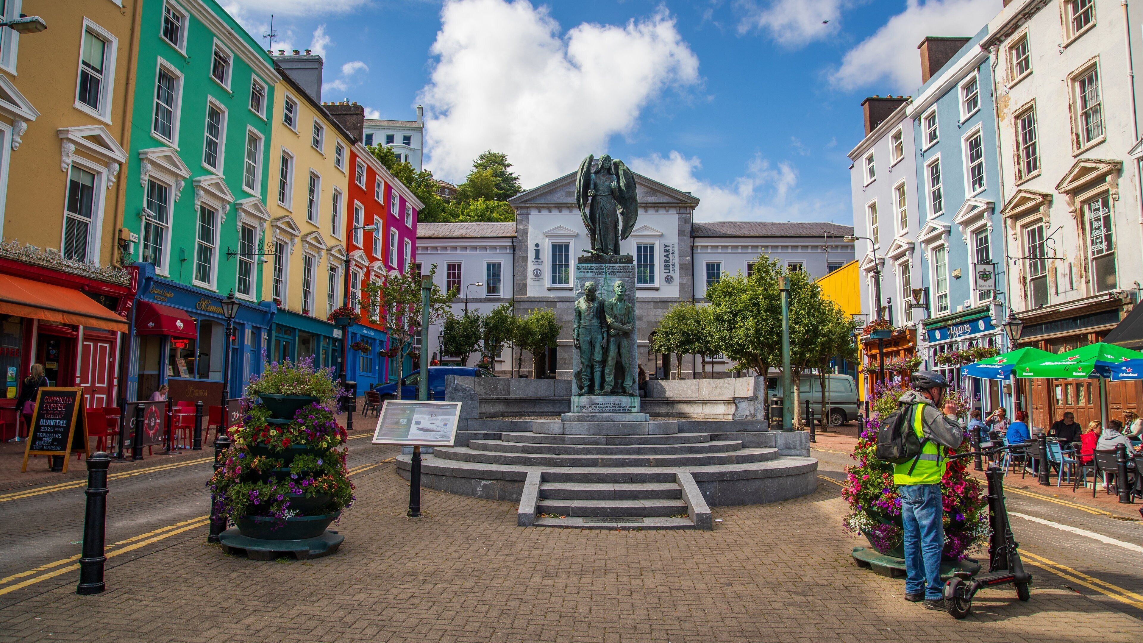 A colorful street with a statue in the center, surrounded by historic buildings and flower pots.