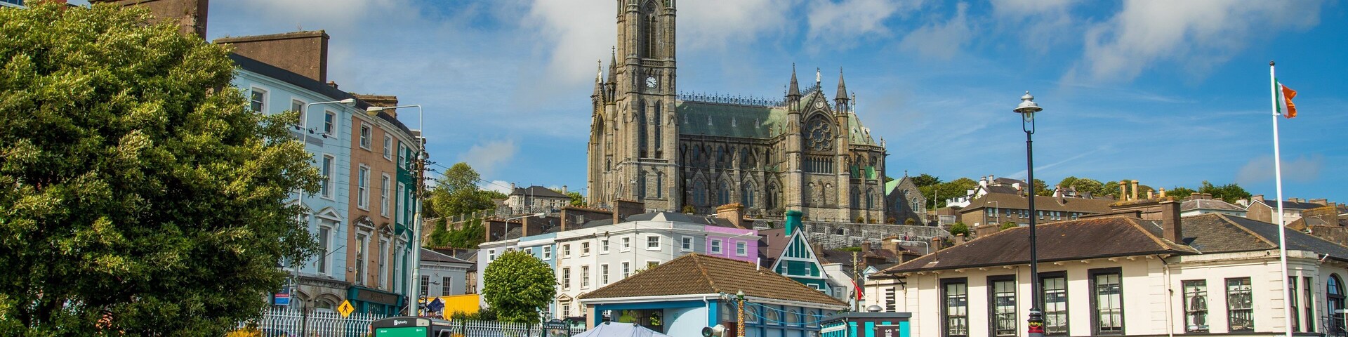 Una catedral histórica con una aguja alta, rodeada de edificios coloridos y una plaza pública con bancos.