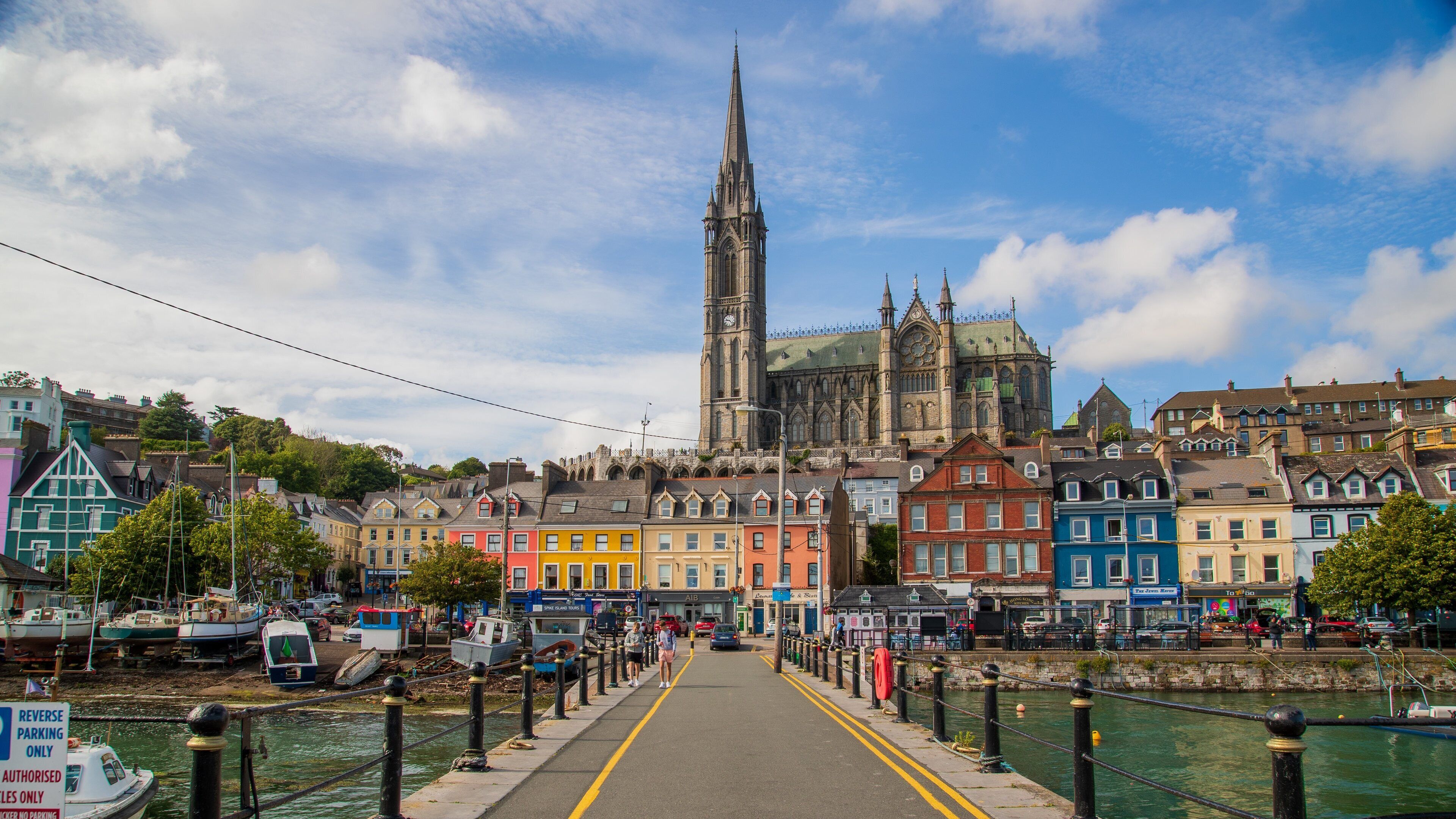 A colorful waterfront town with a prominent church tower and a bridge leading to it.