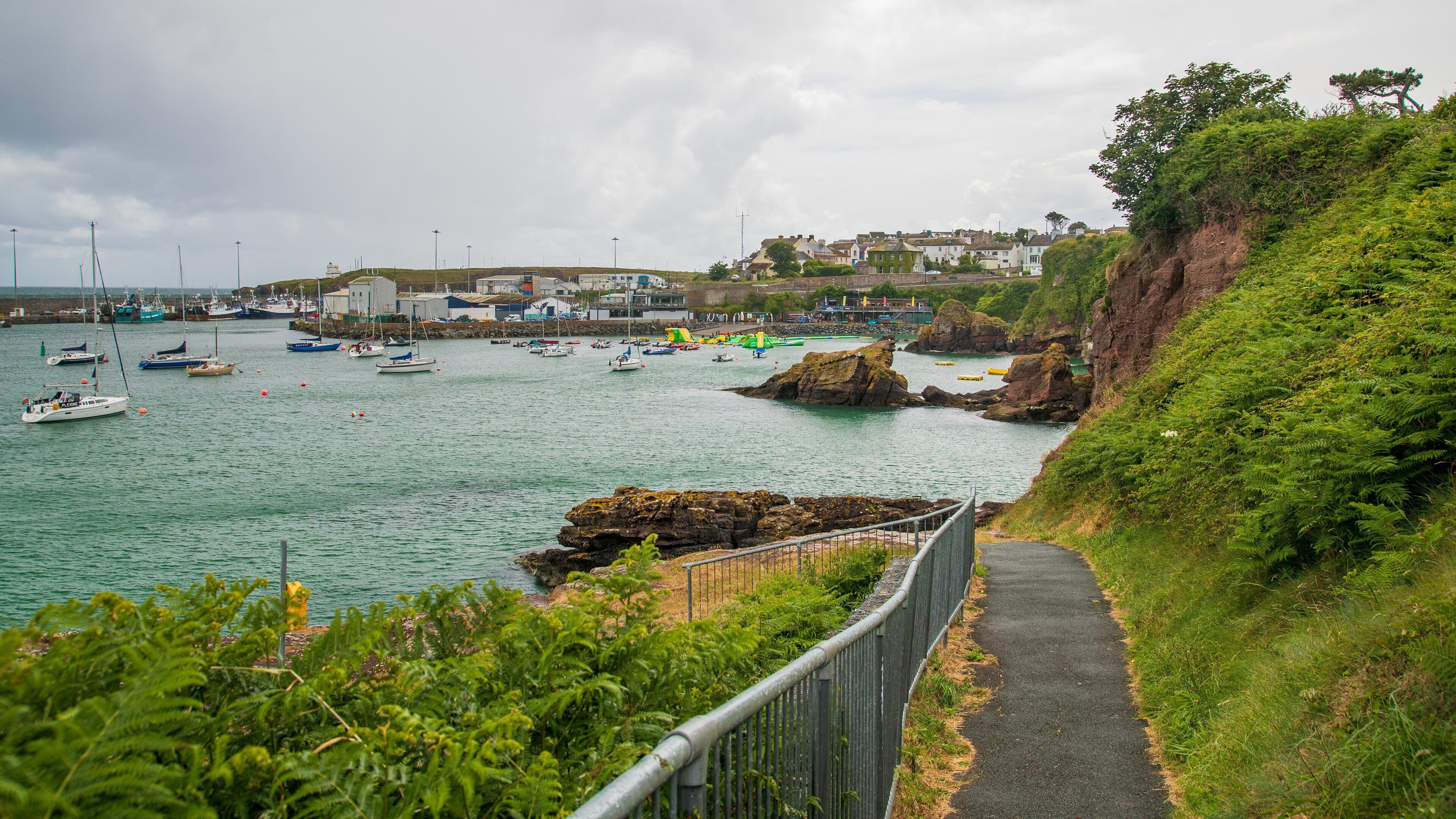 A coastal town with boats, rocky shores, and a path along the cliff.