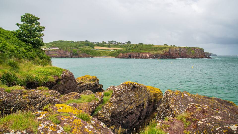A coastal landscape with rocky outcrops, green hills, and a calm sea.