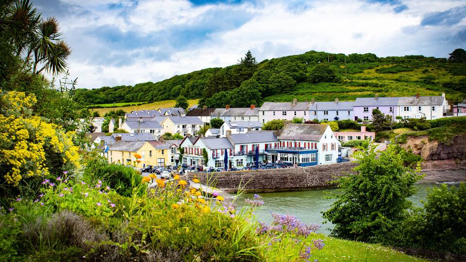 A coastal village with colorful houses by the sea, surrounded by lush greenery and a river.