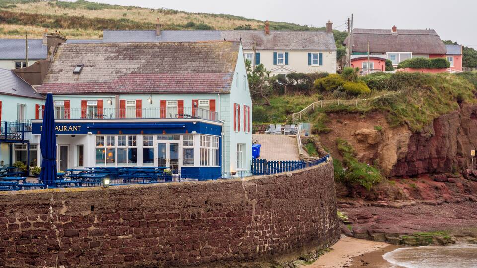 A coastal town with a restaurant named 'Restaurant' and a stone wall along the beach.