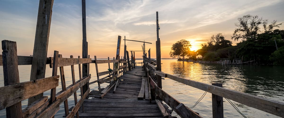 A wooden pier extending into calm water with a sunset in the background.
