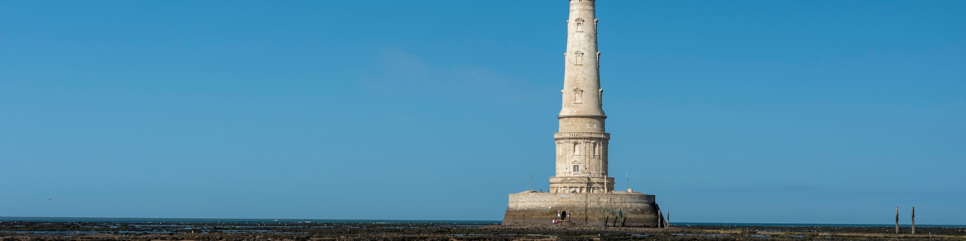 Um farol numa praia arenosa sob um céu azul límpido.