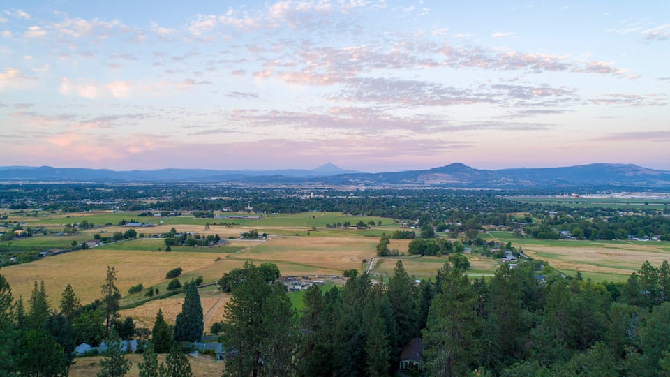 A panoramic view of a valley with a mountain in the distance, surrounded by fields and scattered buildings.