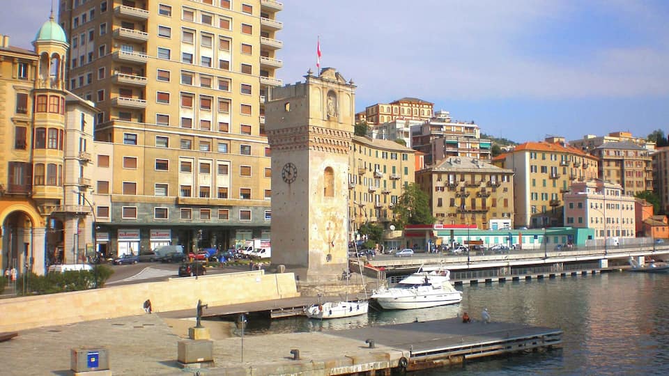 A waterfront cityscape with historic buildings, a prominent clock tower, and a marina with boats.