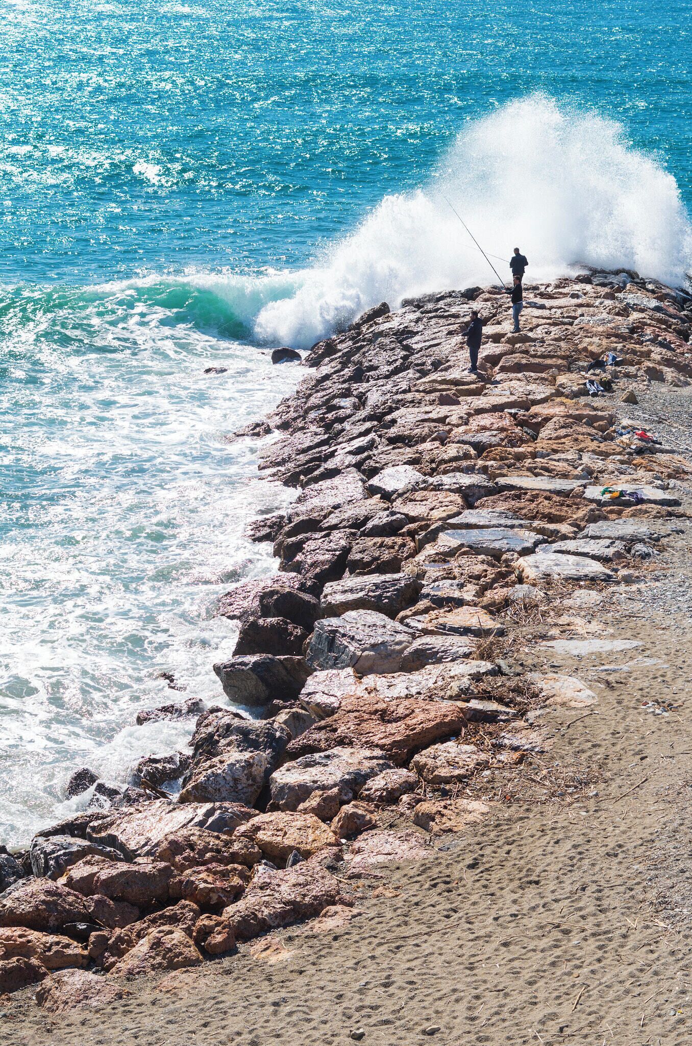 A rocky shoreline with waves crashing against the rocks and a person fishing.