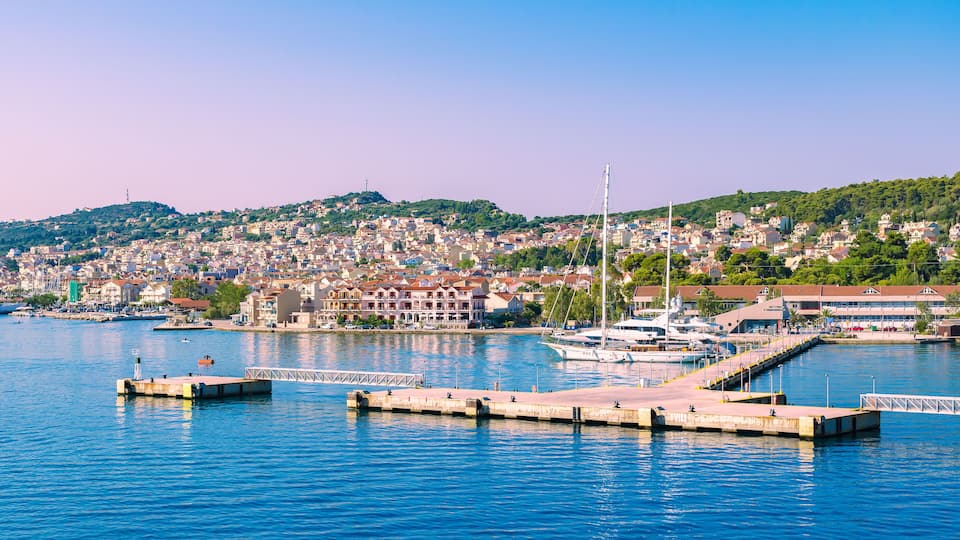 A coastal town with a marina, boats, and a hilly backdrop.