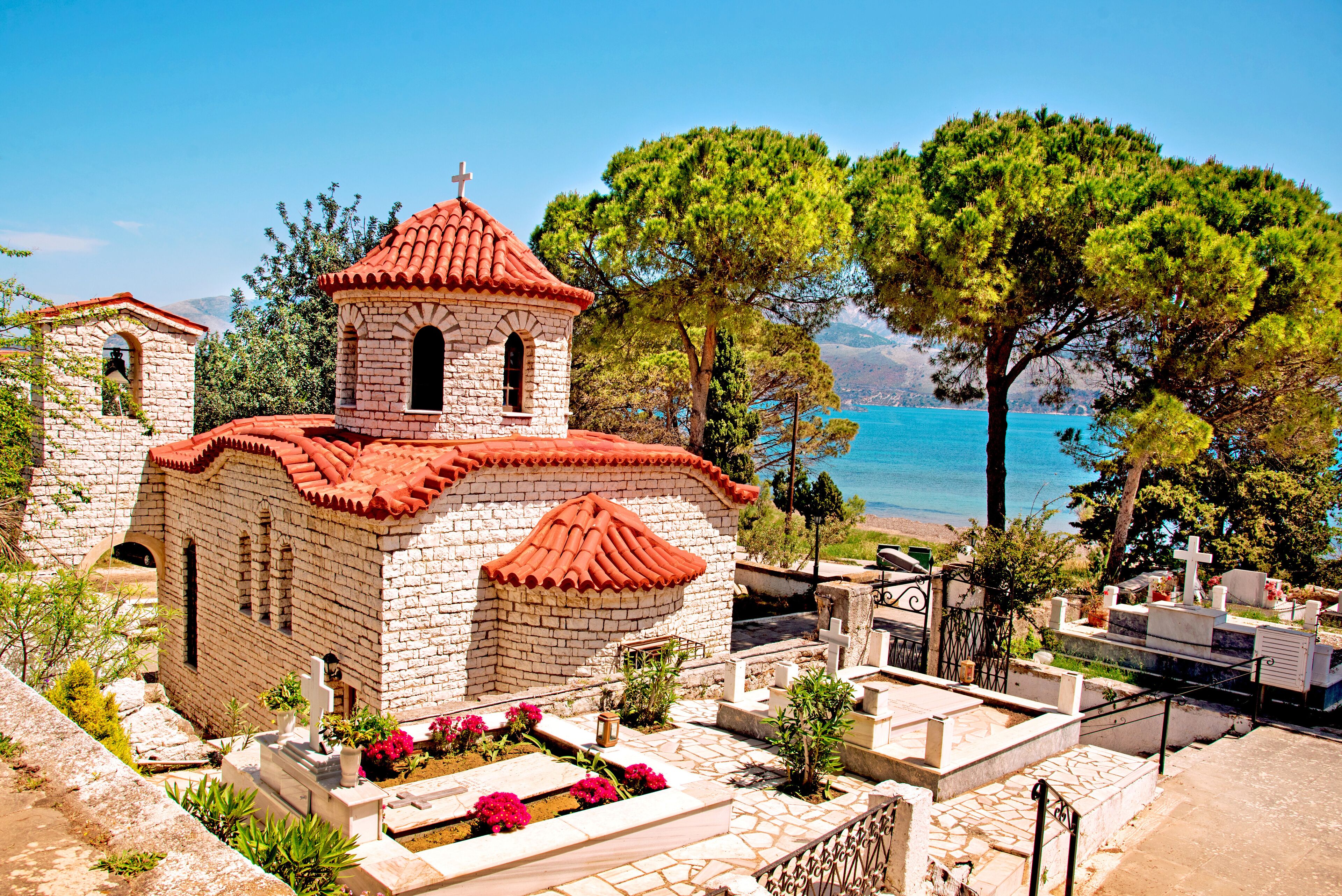 A small church with a red-tiled roof, surrounded by tombs and greenery.