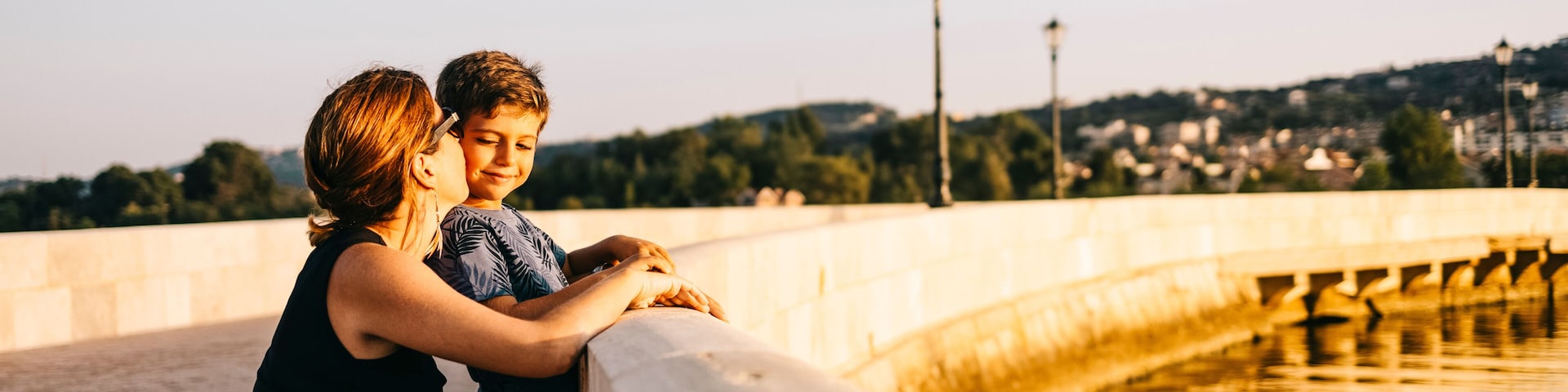 Um casal apoiado no corrimão de uma ponte, com um corpo d'água e edifícios ao longe.