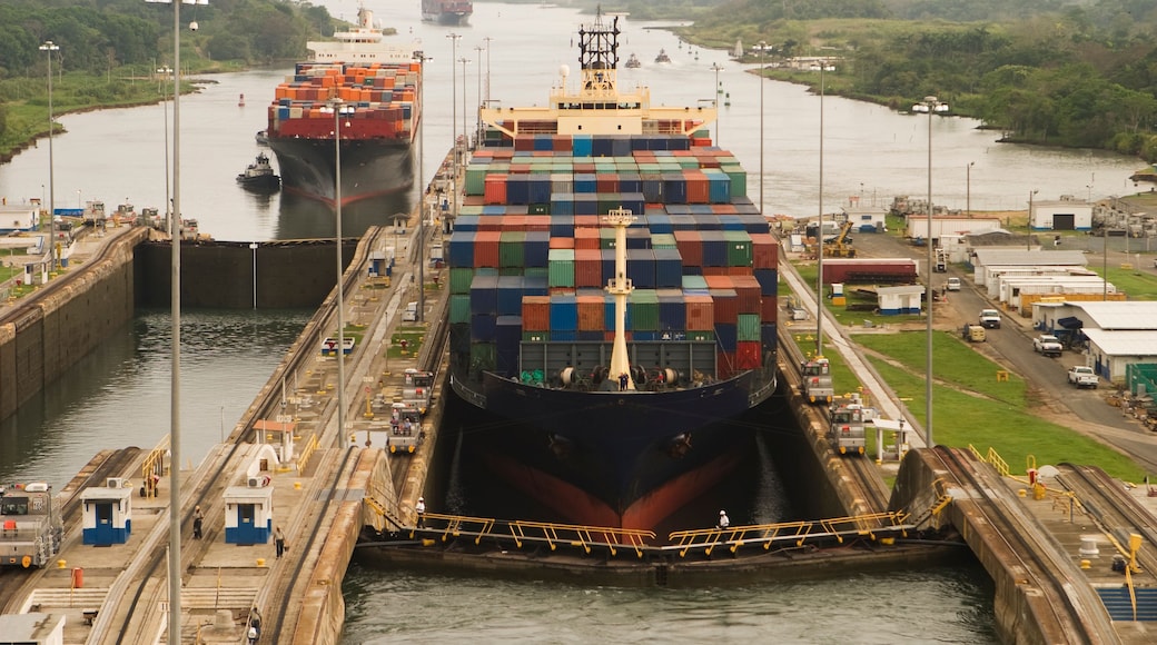 Un buque de carga grande atracado en un puerto con múltiples contenedores apilados en su cubierta.