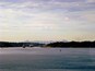 Una masa de agua tranquila con un barco grande, montañas distantes y un cielo nublado.