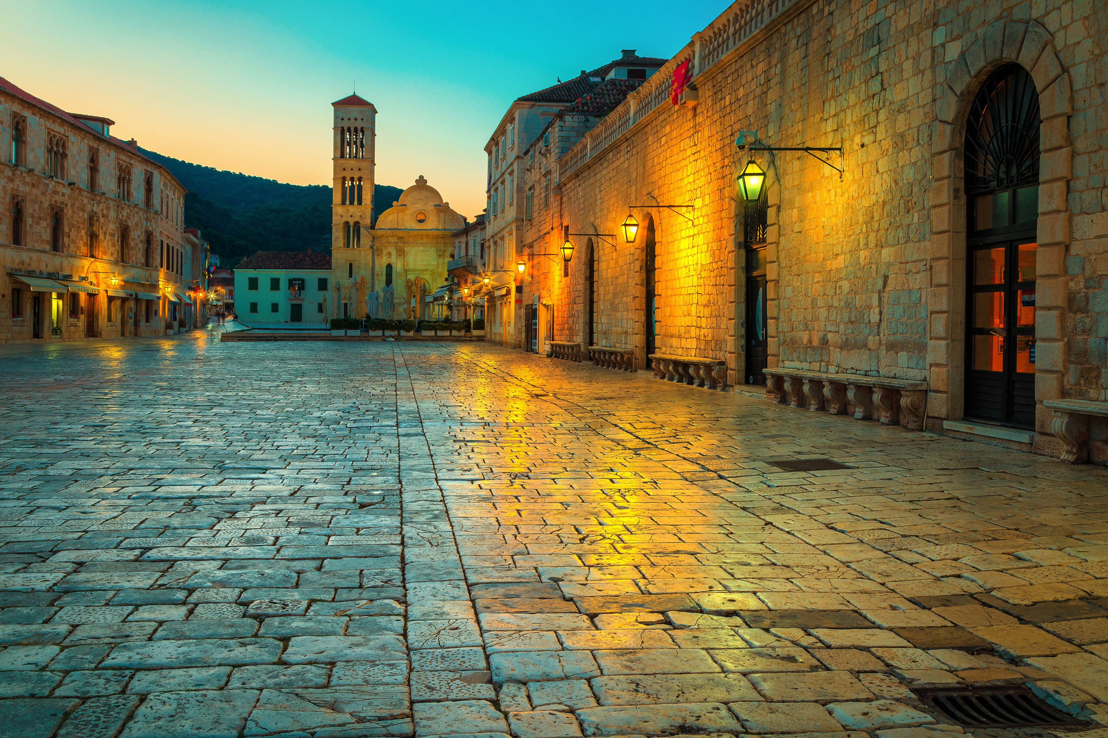 A cobblestone street in a historic town with buildings, a tower, and street lamps.