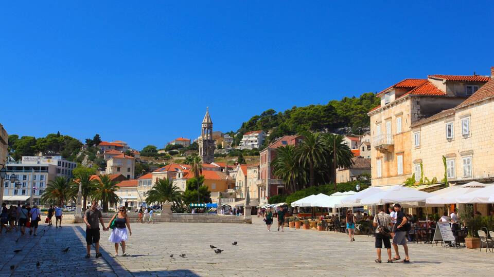 A bustling square with historic buildings, a prominent tower, and outdoor cafes.