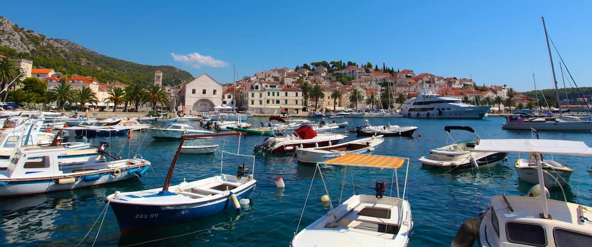 A marina with various boats, a coastal town with historic buildings, and a clear blue sky.