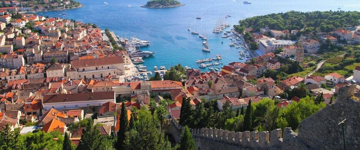 A coastal town with historic buildings, a harbor with boats, and a prominent castle wall.
