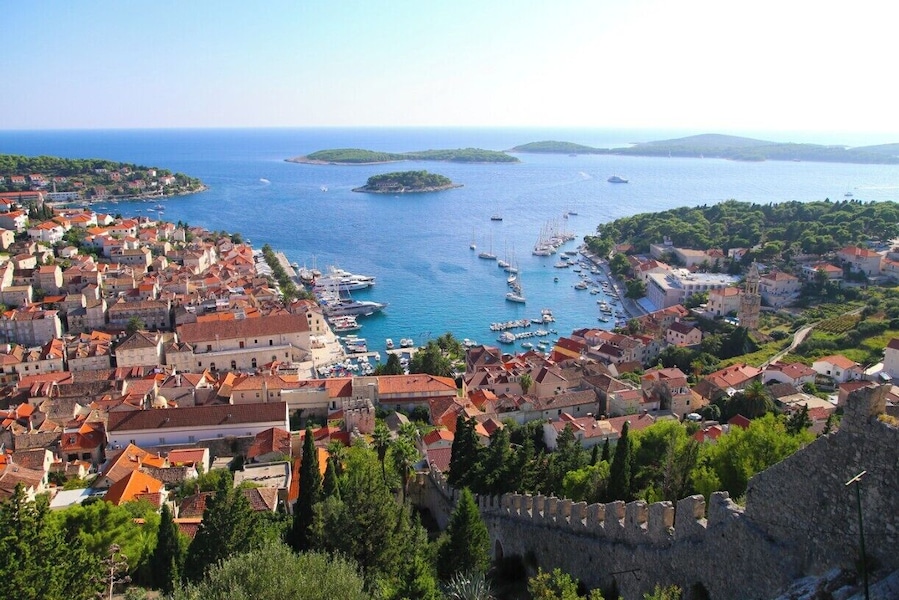 A coastal town with historic buildings, a harbor with boats, and a prominent castle wall.