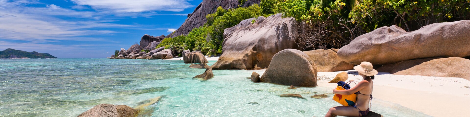 Una playa tropical despejada con rocas grandes, palmeras y una persona sentada sobre una roca.
