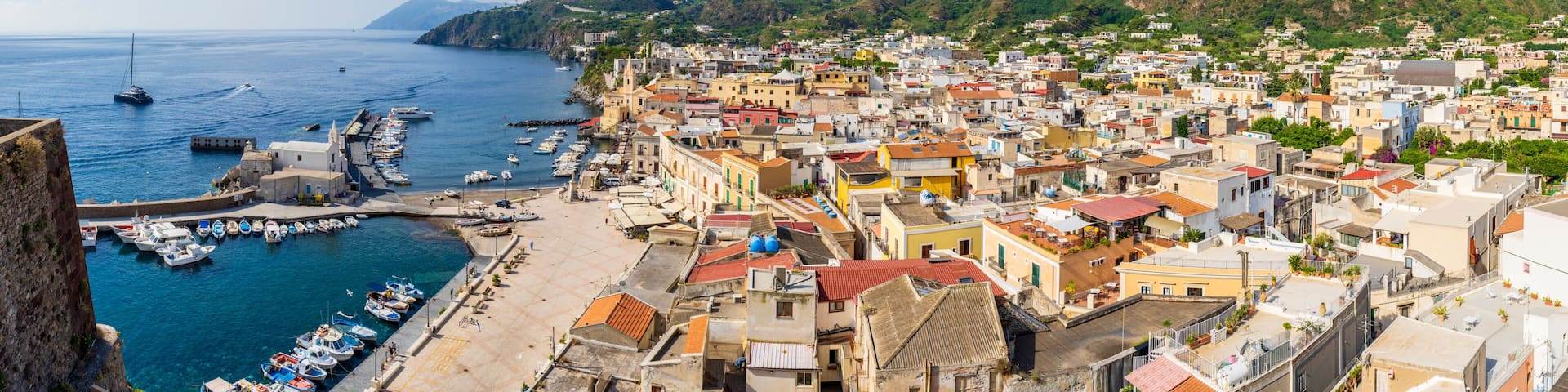 A coastal town with a marina, colorful buildings, and a hill in the background.