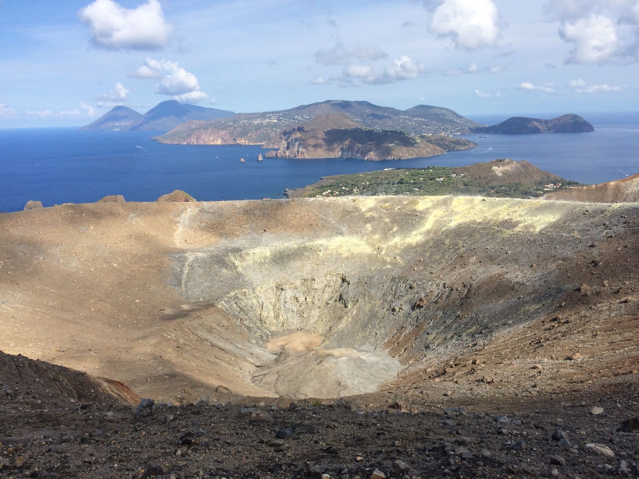 A volcanic landscape with a crater, distant islands, and a clear sky.